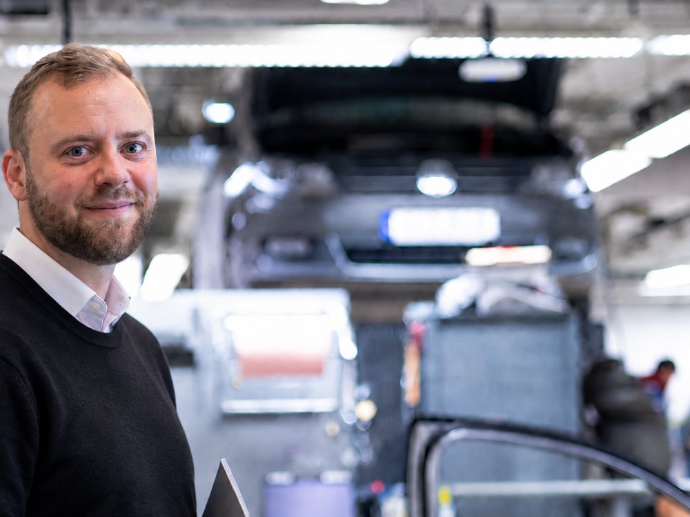 Employee in a workshop with a car raised on a lift in the background